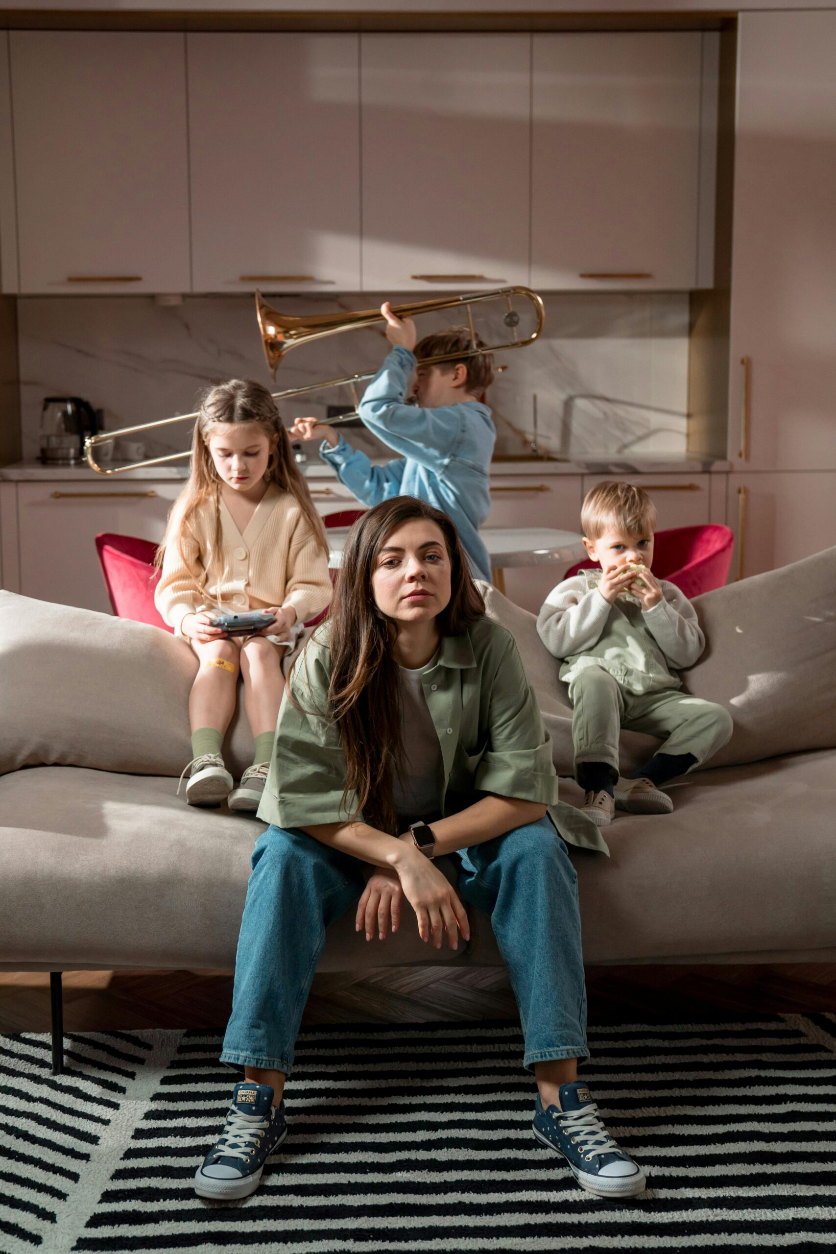 A mother sits with her children playing indoors on a sofa in a modern living room.